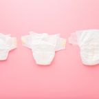 White soft baby diapers on light pink table background. Pastel color. Different sizes. Closeup. Top down view.