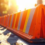 A highly visible orange safety barrier with bright reflective stripes stands under brilliant midday sun, clearly blocking off a hazardous area, essential for public safety and site management.